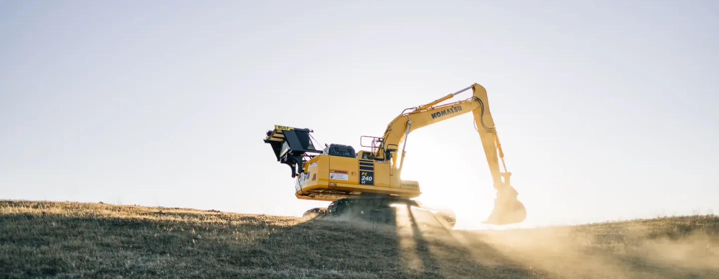 Excavator bekerja di lahan terbuka saat matahari rendah